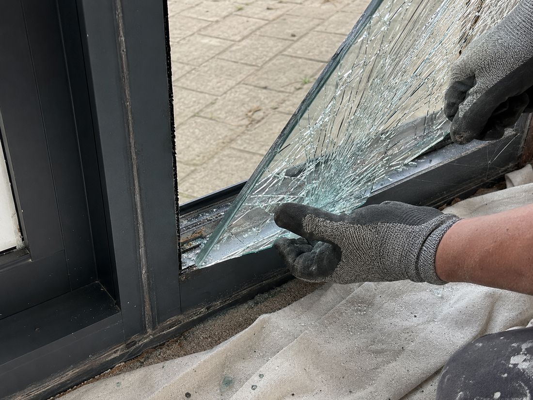 Broken pane being lifted out of a dark aluminium window frame by a glazier in cut resistant gloves