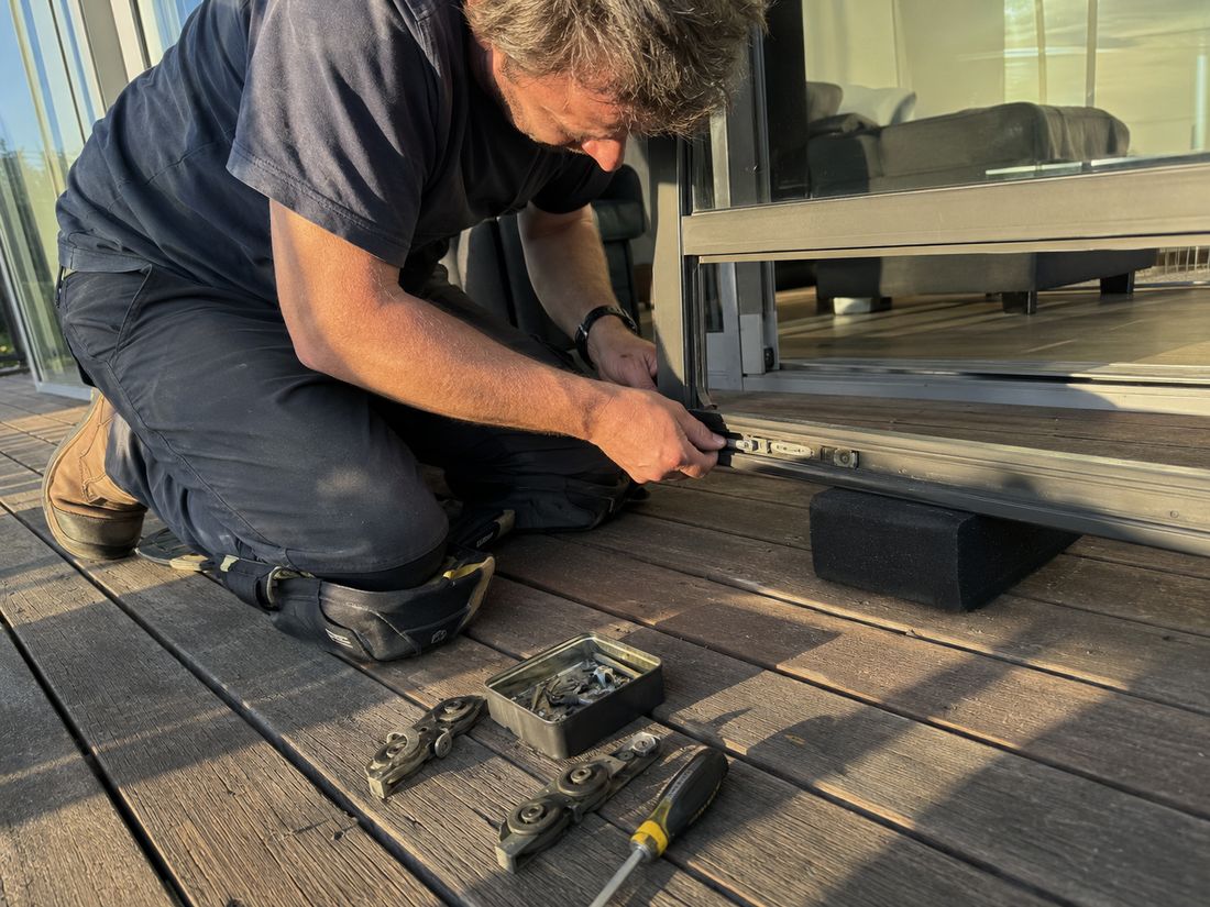 Glazier kneeling on a timber deck replacing the rollers on the bottom rail of an aluminium ranch slider